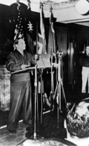 General Douglas MacArthur stands behind a podium speaking to the press.